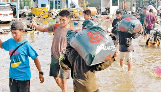  ??  ?? Habitantes de las islas Célebes cargan bolsas con alimentos tras el asalto al centro comercial Matahari.
