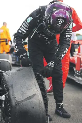  ?? Picture: AFP ?? DISASTER AVERTED. Mercedes’ British driver Lewis Hamilton inspects his damaged tyre in the parc ferme after winning the British Formula One Grand Prix at Silverston­e yesterday.