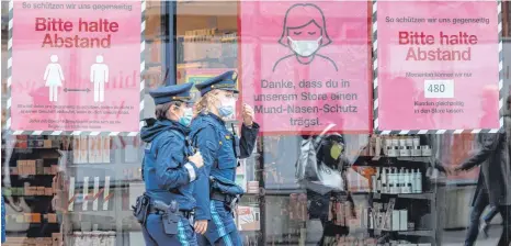  ?? FOTO: PETER KNEFFEL/DPA ?? Polizistin­nen gehen in der Münchner Innenstadt an Schildern vorbei , die zum Tragen von Mund-Nasen-Schutz auffordern.