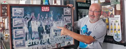  ??  ?? SU PRIMER ENTRENADOR, MUY BLANCO. Carlos García de Cossio posa con el póster de la Séptima, que tiene colgado en su bar.