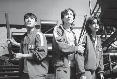  ?? YOUNGKYU PARK/NETFLIX ?? South Korean cast members Park Hae-soo, from left, Lee Jung-jae and Jung Ho-yeon in “Squid Game,” a globally popular South Korea-produced Netflix show that depicts hundreds of financiall­y distressed characters competing in deadly children’s games for a chance to escape severe debt.
