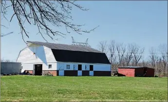  ??  ?? The gothic arched-roof barn has a hayloft door cover and red brick accents near the foundation and white wood plank walls.