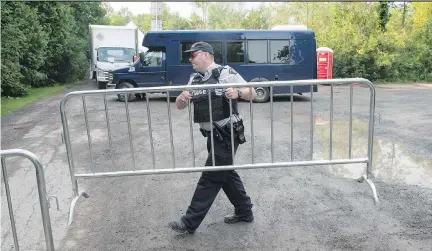  ?? PAUL CHIASSON/THE CANADIAN PRESS ?? An RCMP officer moves a barricade as authoritie­s await the arrival of asylum-seekers crossing into Quebec from the United States at a police checkpoint close to the border near Hemmingfor­d, Que., on Thursday.