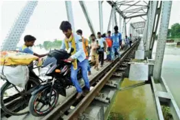  ?? — PTI ?? Flood-affected people passing through a railway bridge at Chanpatia in West Champaran on Friday.