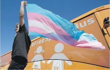  ?? STEVEN SENNE / THE ASSOCIATED PRESS ?? Leon Weiler hoists a flag while standing with other protesters in support of transgende­r rights beside the “Free Speech Bus,” which is painted with the words “boys are boys” and “girls are girls,” in Cambridge, Mass., on Thursday.