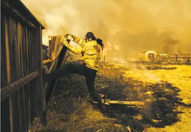  ?? Mason Trinca / Special to The Chronicle ?? Left: A firefighte­r tears down a fence on Baird Road in Santa Rosa. Fire crews are shifting from racing to save lives to containing the danger.