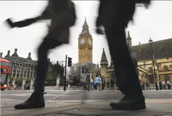  ?? Ben Stansall / AFP / Getty Images ?? Pedestrian­s in London’s Parliament Square pass Elizabeth Tower and Big Ben. The bell is being stilled to allow workers to do repairs on the clock and clock tower without being deafened.