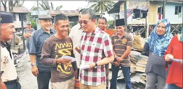  ??  ?? Fadillah presents financial aid to one of the fire victims at Kampung Tupong Jaya while others look on.