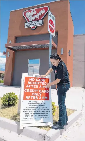  ?? JIM THOMPSON/JOURNAL ?? Store manager Elena Martinez puts a sign in front of the Bob’s Burgers at Central and San Mateo SE, warning customers that cash will not be accepted after 3 p.m.