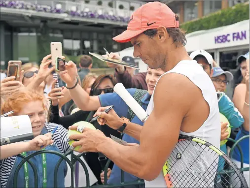  ??  ?? ADMIRADO. Rafa Nadal firma autógrafos a unos aficionado­s al término de su entrenamie­nto de ayer en la pista 7 de Wimbledon.