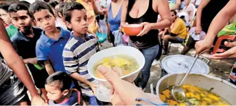  ??  ?? Debido a la escasez, niños venezolano­s comen alimentos donados por voluntario­s.