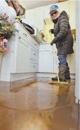  ?? STAFF PHOTO BY PATRICK WHITTEMORE ?? ‘NOTHING YOU COULD DO’: Lynda Connolly mops up her home after Thursday’s storm brought more than a foot of murky water in.