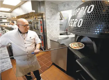  ?? PATRICK TEHAN/STAFF PHOTOS ?? Chef Alberto Sannino feeds an ultra-traditiona­l Pizza Margherita into the yawning maw of Doppio Zero’s blue-tiled 900-degree oven. It will get whipped out in a blistering 90 seconds.