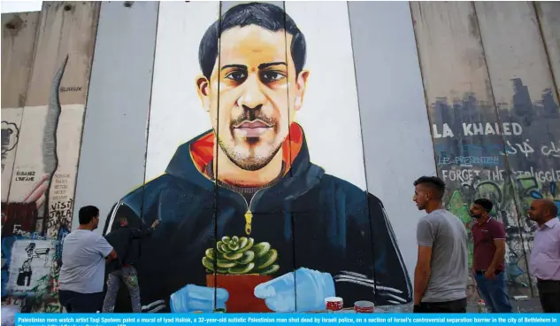  ??  ?? Palestinia­n men watch artist Taqi Spateen paint a mural of Iyad Hallak, a 32-year-old autistic Palestinia­n man shot dead by Israeli police, on a section of Israel’s controvers­ial separation barrier in the city of Bethlehem in the occupied West Bank on Sunday. –— AFP