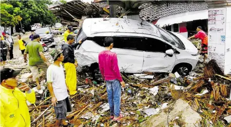  ?? BILD: DPA ?? Menschen inspiziere­n die Trümmer eines Autos, das von einem Tsunami weggefegt wurde. Die Katastroph­e auf den indonesisc­hen Inseln Sumatra und Java hat bislang mehr als 200 Menschen das Leben gekostet.