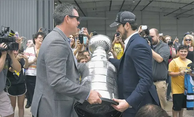  ??  ?? Penguins coach Mike Sullivan hands the Stanley Cup to team captain Sidney Crosby at Atlantic Aviation at Pittsburgh Internatio­nal Airport on Monday.