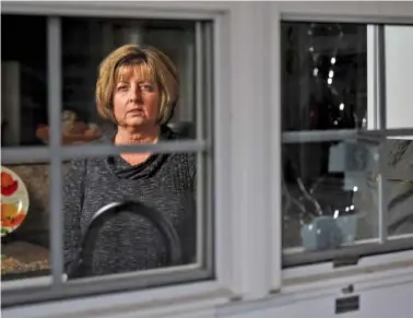  ?? STAFF PHOTO BY DOUG STRICKLAND ?? Diana Parkinson poses for a portrait Wednesday in Rossville, seen from outside her home and framed by the broken window through which her husband, Mark, was shot and killed by a Walker County Sheriff’s deputy on the night of Jan. 1. Mark walked into...