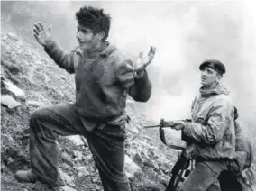  ?? ?? With hands raised, Agustinds Efstathios, 22, climbs the mountainsi­de from his EOKA hideout on March 3, 1957, under the gun of a British soldier of the Duke of Wellington regiment after he surrendere­d with three others when the cave they were hiding in was surrounded by British troops. A fifth man, Gregoris Pieri Afxentios, second-in-command to EOKA leader Georgios Grivas, refused to surrender and fought until he was killed by a blast in the cave hidden in a deep valley of the Trodos mountains of Cyprus, a mile from the isolated monastery of Macheras.