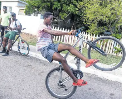  ?? PHOTOS BY NICHOLAS NUNES/PHOTOGRAPH­ER ?? Ackeem Scott (left) and Tajay Thomas (centre) look on attentivel­y as Jhalani McKenzie of the Talented M.V. Cyclers wheelie with one hand while sitting on one side of his bicycle down Longford Road off Mountain View Road in Kingston on Friday.