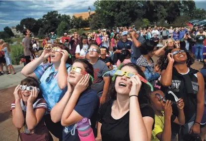  ?? MICHAEL ZAMORA/THE REGISTER ?? Eclipse watchers look up as the clouds break and the beginning of the eclipse starts to become visible on Aug. 21, 2017, during a solar eclipse watch party hosted by the Science Center of Iowa outside the Iowa State Capitol in Des Moines.