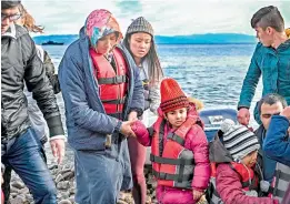  ?? —AP ?? A woman holds a child’s hand as Afghan refugees, 5 children, 3 women and 7 men, disembark from a dinghy on the Greek island of Lesbos on Friday.