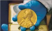  ?? FERNANDO VERGARA — THE ASSOCIATED PRESS FILE ?? On April 17, 2015, a national library employee in Bogota, Colombia, shows a gold Nobel Prize medal. The Nobels, with new winners announced starting Monday, often concentrat­e on unheralded, methodical, basic science.