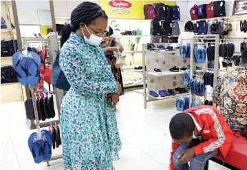  ?? ?? Mrs Bernadette Makhasa watches as her son Ian Matangira tries on a pair of shoes at a shop in Harare yesterday ahead of schools opening on Monday. – Picture: Memory Mangombe
