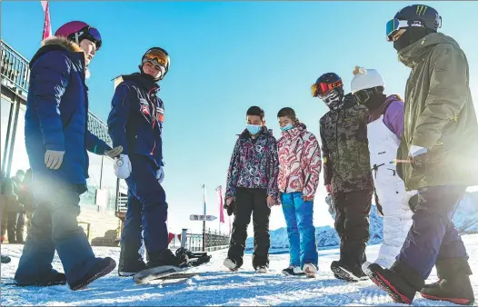  ??  ?? Xu Xiujuan (first from left) explains the basic movements of snowboardi­ng to students who participat­e in the free public class at Xinjiang Baiyun Internatio­nal Ski Resort.