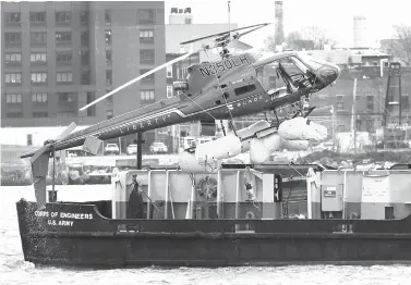  ?? Associated Press ?? ■ A helicopter is hoisted by crane from the East River onto a barge Monday in New York. The pilot was able to escape the Sunday night crash after the aircraft flipped upside down in the water, killing several passengers, officials said.