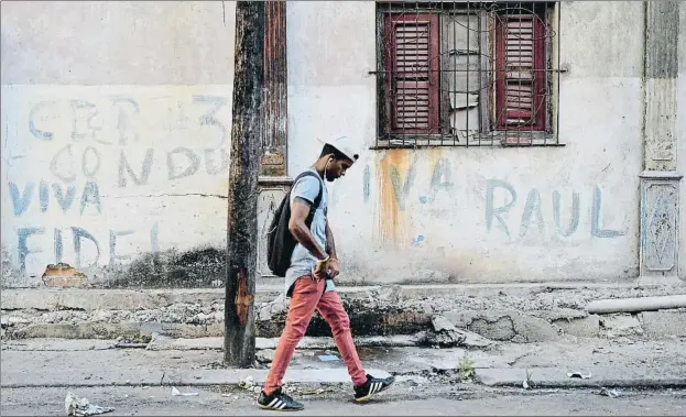  ?? YAMIL LAGE / AFP ?? Mensajes del
pasado. Un joven camina por una calle de La Habana junto a unas pintadas ya gastadas con vivas al desapareci­do Fidel Castro y a su hermano Raúl, que aunque retirado a un segundo plano sigue gobernando el timón