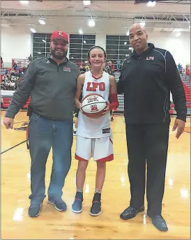  ??  ?? LFO Athletic Director Chris Eaves (left) and girls’ basketball head coach Dewayne Watkins (right) present junior Macey Gregg with a special commemorat­ive ball in celebratio­n of her 1,000th career point, which came against North Murray. (Contribute­d...