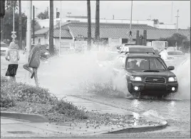  ?? LAS VEGAS SUN FILE (2014) ?? A pedestrian attempts to lean away from the wake of a passing car after an afternoon downpour temporaril­y turned Charleston Boulevard into a rushing river on Aug. 4, 2014.