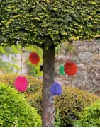  ??  ?? Wool pom-poms hang like baubles from a yew umbrella (left). Painted tyres, used as containers for planting potatoes, add more splashes of colour around stone steps (right).
