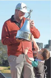  ?? ASSOCIATED PRESS ?? Marc Leishman holds the championsh­ip trophy as his son Oliver, 3, jumps up to slap it.