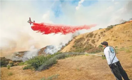  ?? Paul Rodriguez, The Orange County Register ?? Aaron Funk waters the hillside behind his parents’ home north of Los Angeles as a plane drops retardant during a wildfire last summer in Southern California.