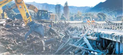  ?? Photo / Alan Gibson ?? Contractor­s work to clear the huge amounts of forestry debris that have damaged the Wigan Bridge.