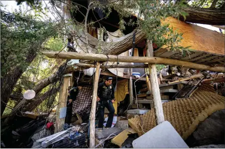  ?? WATCHARA PHOMICINDA — STAFF PHTOOGRAPH­ER ?? Riverside Police officers JC Cuevas, center, and Justin Mann, left, survey a homeless encampment in the Santa Ana River bed in Riverside on Friday.