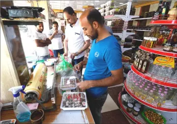  ??  ?? An Iraqi merchant wraps up a package of sweets at a shop selling dates and other date-related products in the region of Abu al-Khasib.