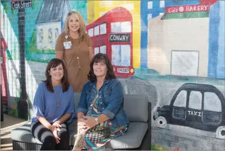  ?? WILLIAM HARVEY/RIVER VALLEY & OZARK EDITION ?? Donna Beshears, left, activity therapist for the Conway Regional Senior Behavioral Health Unit, sits with artist Jan Mallett of Conway in front of the mural Mallett painted on the unit’s patio. Standing is Dot Welch, associate director of the Conway...