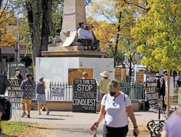  ?? LUIS SÁNCHEZ SATURNO/THE NEW MEXICAN ?? Two men sit chained to the Plaza obelisk Saturday. They are among a group of protesters who want the mayor to keep his promise to take the obelisk down.