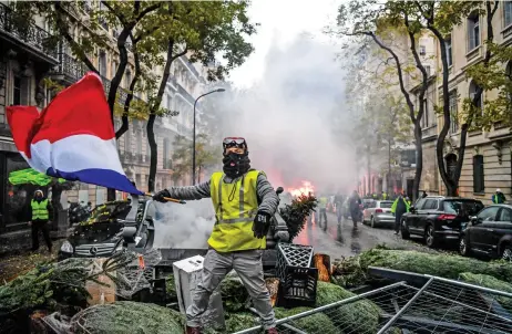  ?? (AFP) ?? A demonstrat­or holds a French flag among christmas trees during a protest of Yellow Vests (Gilets Jaunes) against rising oil prices and living costs, in Paris