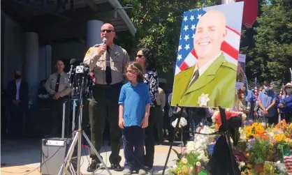  ?? Photograph: Martha Mendoza/AP ?? The Santa Cruz sheriff, Jim Hart, stands next to a photo of fallen Sgt Damon Gutzwiller, who was shot and killed in Ben Lomond.