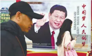 ?? AFPPIX ?? People walk past a poster of Xi beside a street in Beijing yesterday.
