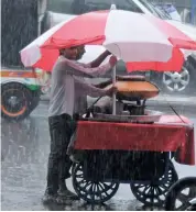  ?? — BIPLAB BANERJEE ?? A group of girls (left) use an umbrella during a heavy downpour in New Delhi on Wednesday. A street vendor (above) during the rain. Delhiites got a temporary relief from the scorching sun on after the city experience­d a variation of heavy to light...