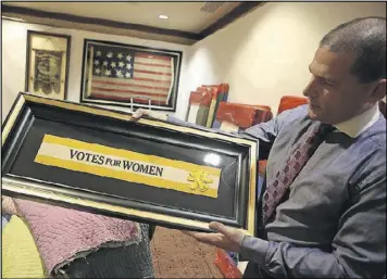  ?? HENRY TAYLOR / HENRY.TAYLOR@AJC.COM ?? At the 2017 Cathedral Antiques Show in Atlanta, Jeff Bridgman shows off a piece of a sash that had been worn during the women’s suffrage movement in the early 20th century.