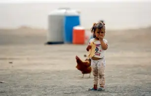  ??  ?? A displaced child stands outside a camp for displaced families near the town of Al Karamah. —