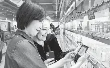  ?? Courtesy of CJ Olive Young ?? A clerk at CJ Olive Young’s store in Myeong-dong, Seoul, left, helps a customer with the company’s new portable translatio­n device, Thursday.