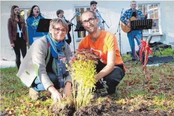  ?? FOTO: SIMON NILL ?? Bürgermeis­terin Christina Schnitzler (links) und Michael Gretz beim ersten Einpflanze­n einer blühenden Staude im Mitmach-Garten. Im Hintergrun­d: Teile der Band „Noir Blanc“, die während der Feier spielte.