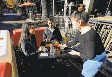  ?? Rich Pedroncell­i Associated Press ?? RESTAURANT­S have ramped up outdoor seating, takeout and delivery options amid the pandemic. Above, server Tami Bat, right, brings drinks to Ranim Abaad, left, and Joey Bettencour­t on Friday in Sacramento.