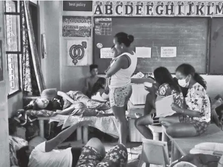  ?? AP/AARON FAVILA ?? RESIDENTS stay inside a dimly-lit classroom during a power interrupti­on inside a school that was converted into an evacuation center after floods inundate villages in Marikina City due to Typhoon Ulysses on Thursday, November 12, 2020.